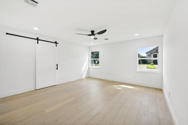 unfurnished room with a barn door, ceiling fan, and light hardwood / wood-style floors