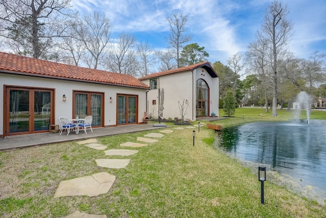 back of property with french doors, a yard, and a water view