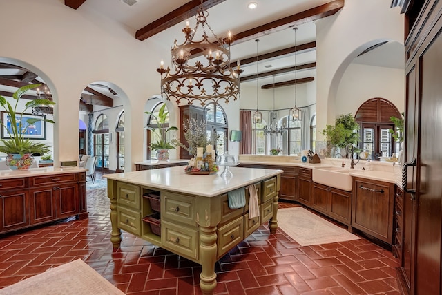 kitchen with sink, a high ceiling, beamed ceiling, pendant lighting, and a kitchen island