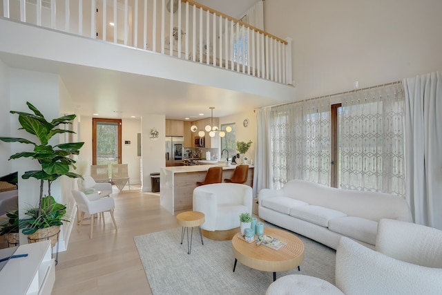 living room featuring a notable chandelier, light wood-type flooring, sink, and a high ceiling