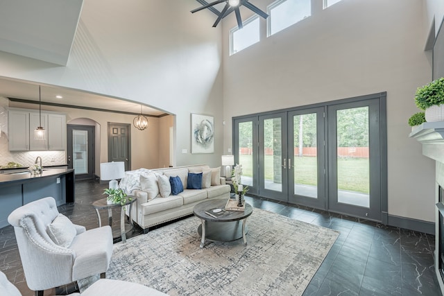 living room with french doors, ceiling fan with notable chandelier, a towering ceiling, and a healthy amount of sunlight