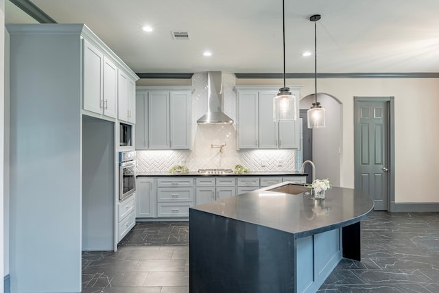 kitchen with an island with sink, white cabinets, wall chimney exhaust hood, sink, and pendant lighting