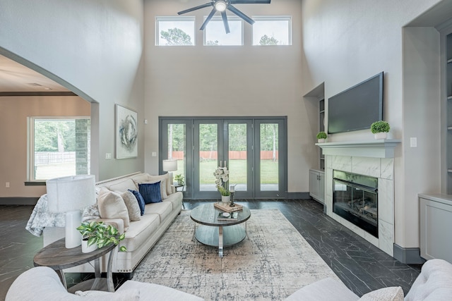 living room featuring a high ceiling, ceiling fan, a wealth of natural light, and a tile fireplace