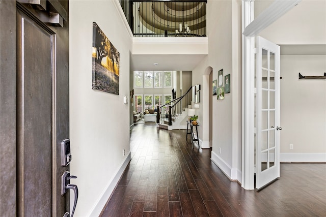 corridor with a towering ceiling, dark hardwood / wood-style floors, and french doors