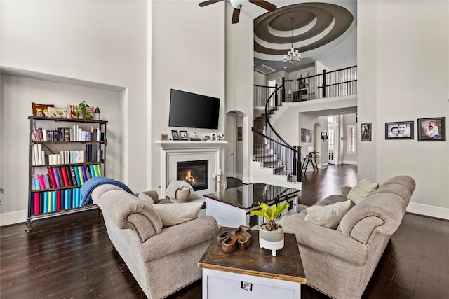 living room featuring ceiling fan with notable chandelier, dark wood-type flooring, a raised ceiling, and a high ceiling