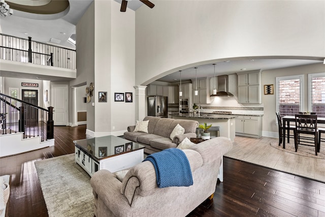 living room with a high ceiling, dark hardwood / wood-style flooring, sink, ceiling fan, and ornate columns