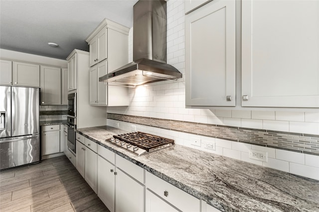 kitchen featuring appliances with stainless steel finishes, light stone countertops, wall chimney exhaust hood, dark wood-type flooring, and decorative backsplash