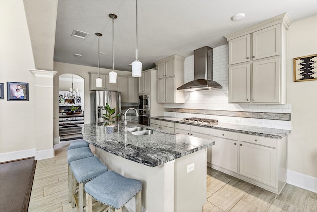 kitchen featuring light hardwood / wood-style flooring, a kitchen breakfast bar, appliances with stainless steel finishes, a center island with sink, and wall chimney range hood