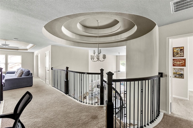 hallway featuring a tray ceiling, carpet floors, a notable chandelier, and a textured ceiling