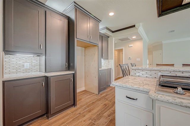 kitchen featuring light stone countertops, ornamental molding, tasteful backsplash, and light hardwood / wood-style flooring