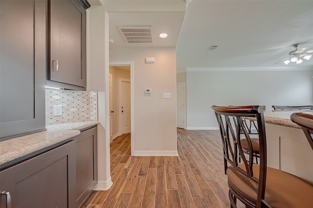 kitchen with gray cabinetry, crown molding, light hardwood / wood-style flooring, ceiling fan, and tasteful backsplash