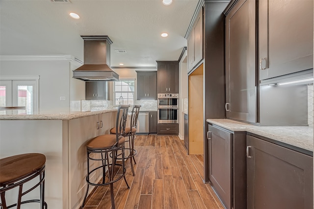 kitchen featuring a kitchen breakfast bar, light stone countertops, light hardwood / wood-style flooring, custom range hood, and crown molding