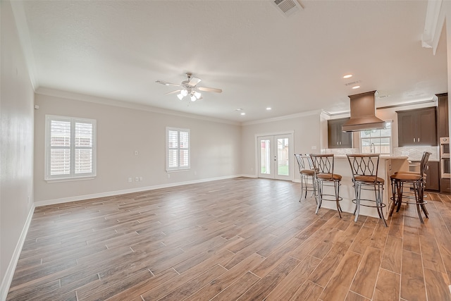 interior space featuring light wood-type flooring, ceiling fan, a breakfast bar, french doors, and custom range hood