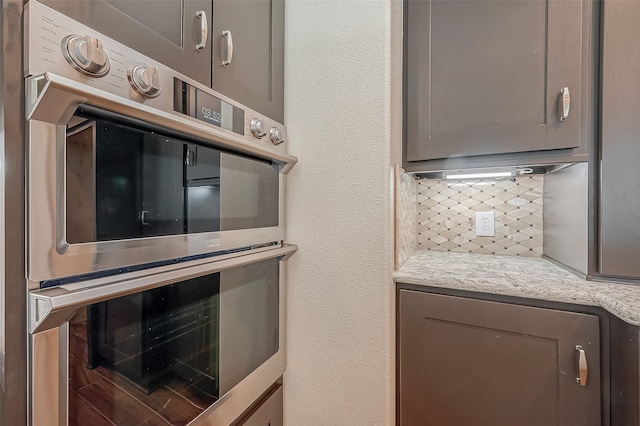 kitchen featuring gray cabinets, stainless steel double oven, and light stone counters