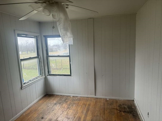 empty room featuring wood walls, ceiling fan, and wood-type flooring