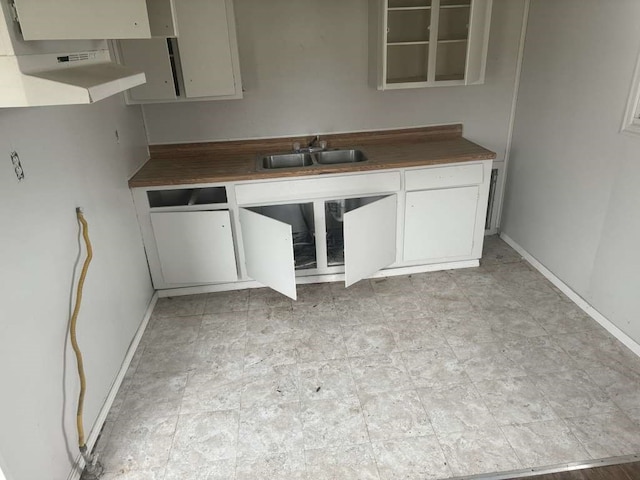 kitchen with butcher block countertops, white cabinetry, and sink