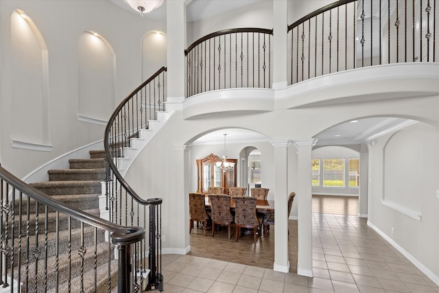 tiled entryway featuring ornamental molding, a towering ceiling, a chandelier, and decorative columns