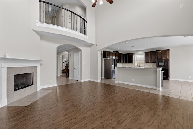 unfurnished living room with a tiled fireplace, a high ceiling, light hardwood / wood-style flooring, ceiling fan, and sink