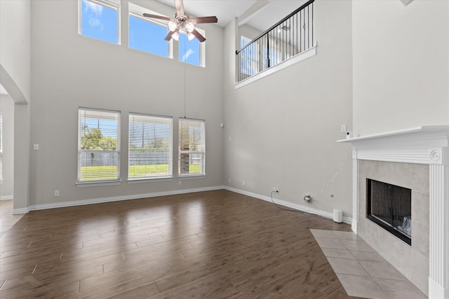 unfurnished living room featuring ceiling fan, hardwood / wood-style floors, a tiled fireplace, and a high ceiling