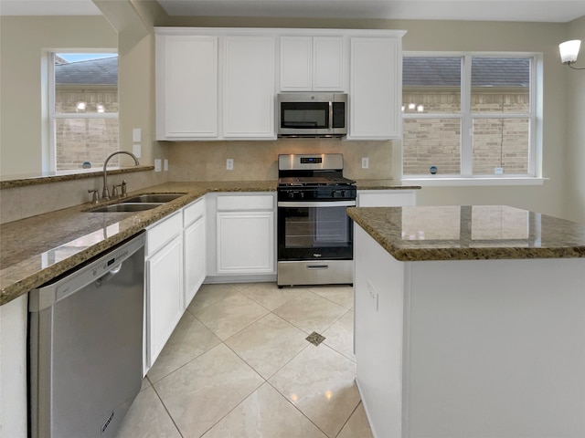 kitchen with stone counters, stainless steel appliances, white cabinetry, sink, and light tile patterned flooring