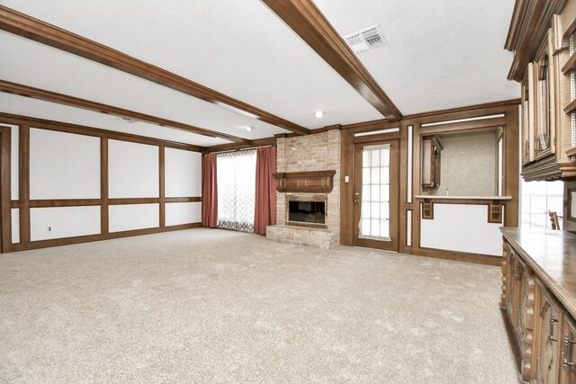 unfurnished living room featuring a brick fireplace, light carpet, beam ceiling, and a wealth of natural light