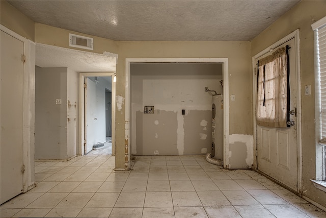 foyer with a textured ceiling, light tile patterned floors, and electric water heater