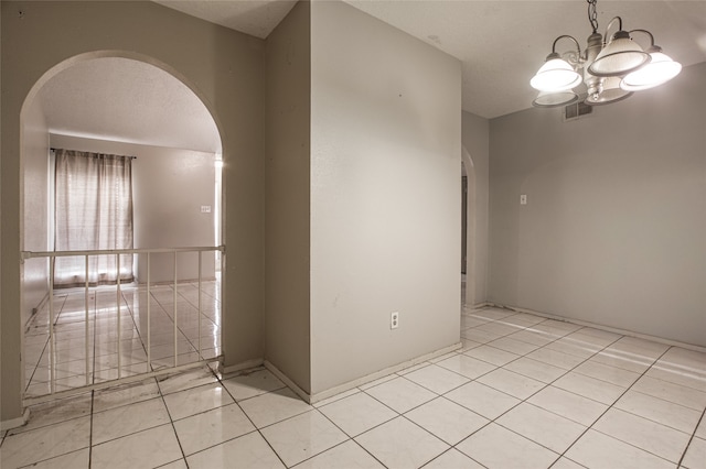 spare room with light tile patterned floors, an inviting chandelier, and a textured ceiling