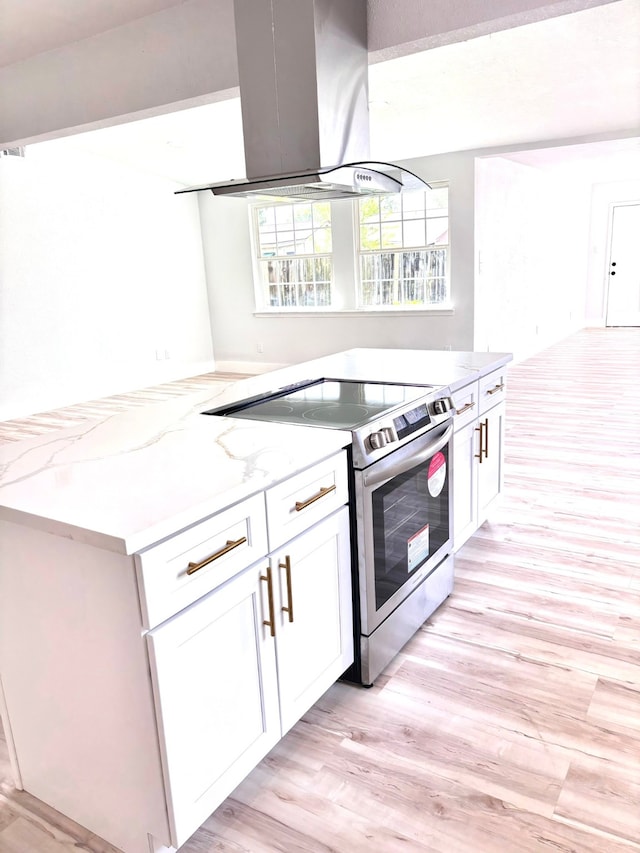 kitchen with stainless steel range with electric stovetop, light wood-type flooring, white cabinetry, exhaust hood, and light stone countertops