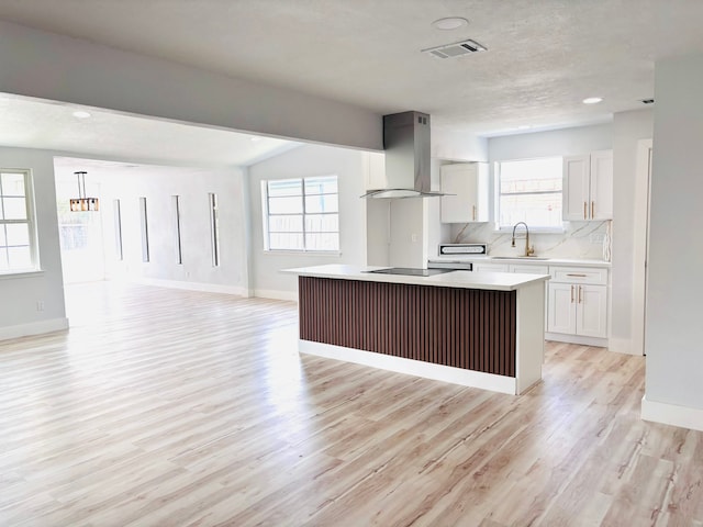 kitchen with white cabinets, light hardwood / wood-style floors, a center island, and wall chimney exhaust hood