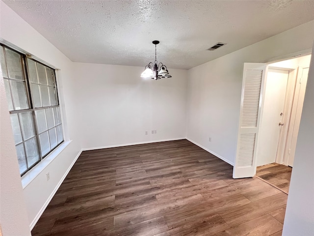 spare room with a textured ceiling, dark wood-type flooring, and a chandelier