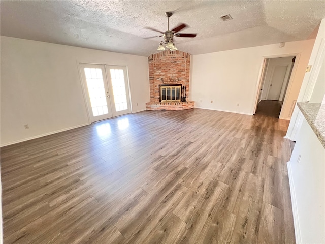 unfurnished living room with a textured ceiling, wood-type flooring, a brick fireplace, ceiling fan, and vaulted ceiling