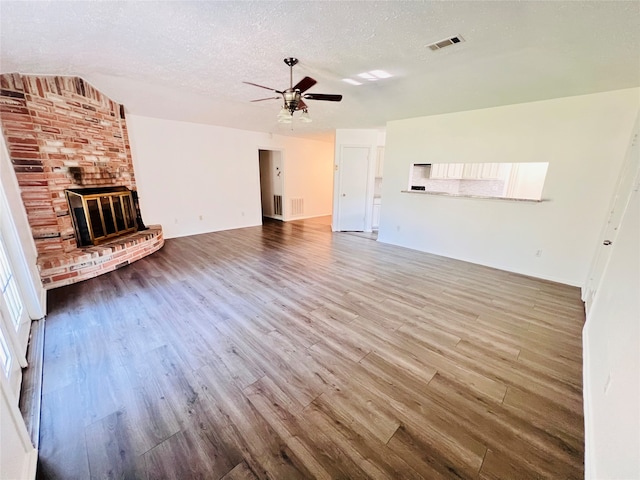 unfurnished living room with a textured ceiling, a brick fireplace, wood-type flooring, and ceiling fan