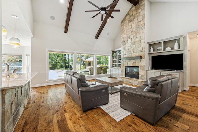 living room with ceiling fan, plenty of natural light, wood-type flooring, and a stone fireplace