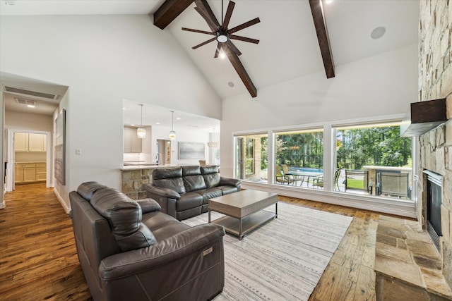 living room with a stone fireplace, wood-type flooring, beam ceiling, high vaulted ceiling, and ceiling fan