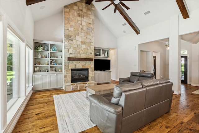 living room featuring light wood-type flooring, ceiling fan, a fireplace, and beamed ceiling