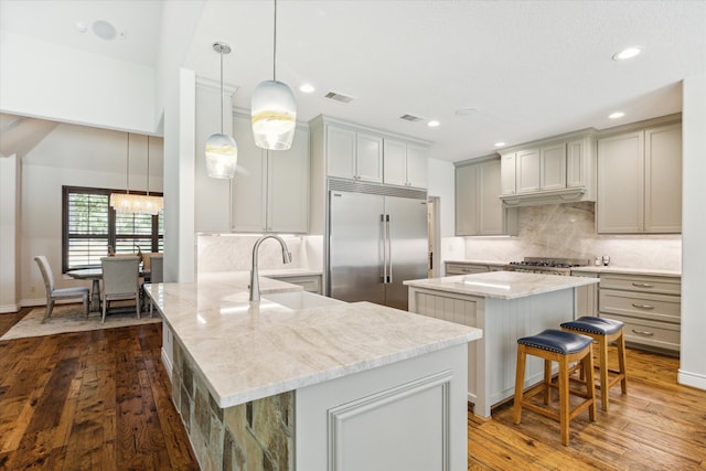 kitchen featuring a kitchen breakfast bar, pendant lighting, a kitchen island with sink, built in refrigerator, and dark wood-type flooring