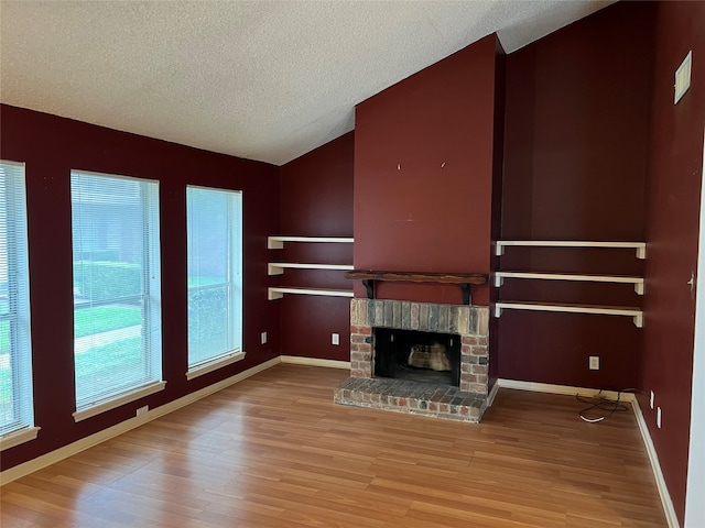 unfurnished living room with a fireplace, a textured ceiling, lofted ceiling, and light hardwood / wood-style floors