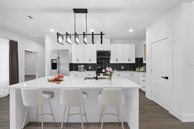 kitchen with a kitchen island with sink, decorative light fixtures, stainless steel appliances, dark hardwood / wood-style floors, and white cabinets