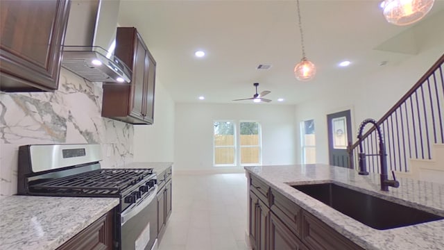 kitchen featuring pendant lighting, sink, wall chimney exhaust hood, gas stove, and light stone counters