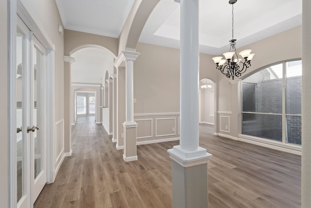 foyer with wood-type flooring, ornamental molding, an inviting chandelier, and ornate columns