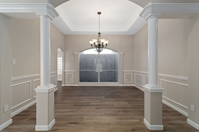 unfurnished dining area featuring dark wood-type flooring, a tray ceiling, decorative columns, and a chandelier