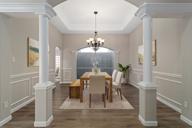 dining area with a tray ceiling, an inviting chandelier, decorative columns, and dark hardwood / wood-style floors