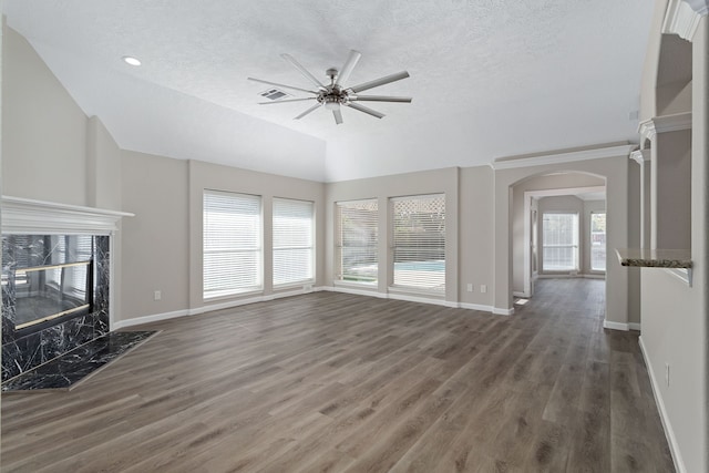 unfurnished living room featuring a high end fireplace, dark wood-type flooring, plenty of natural light, and ceiling fan