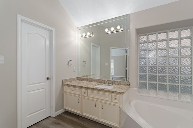 bathroom with lofted ceiling, vanity, hardwood / wood-style flooring, and a washtub