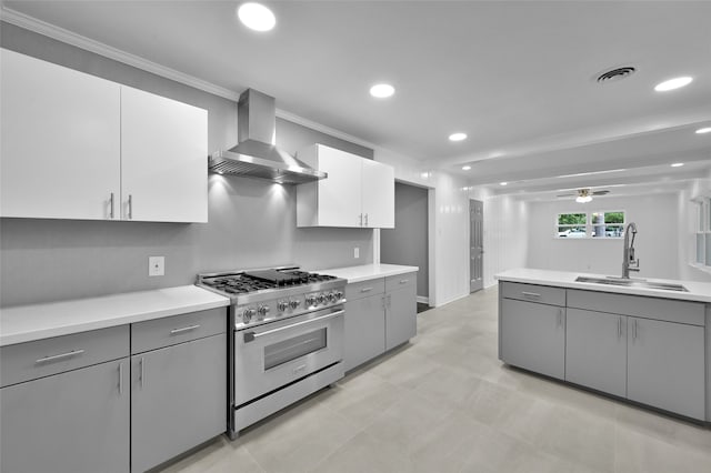 kitchen with stainless steel range, light countertops, gray cabinetry, a sink, and wall chimney range hood