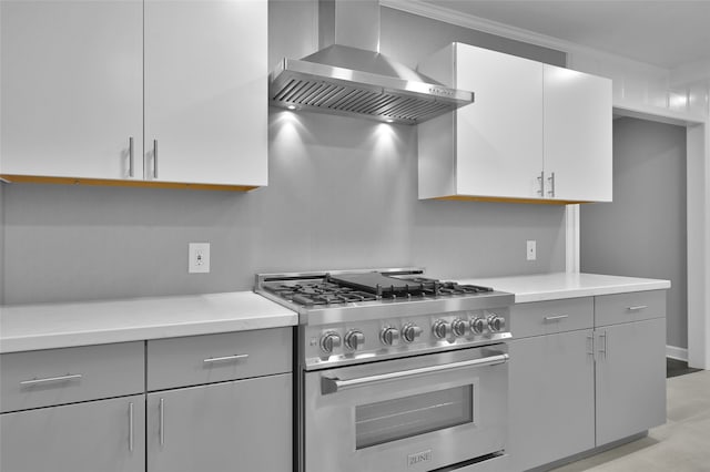 kitchen with wall chimney exhaust hood, high end stainless steel range, light countertops, and gray cabinetry