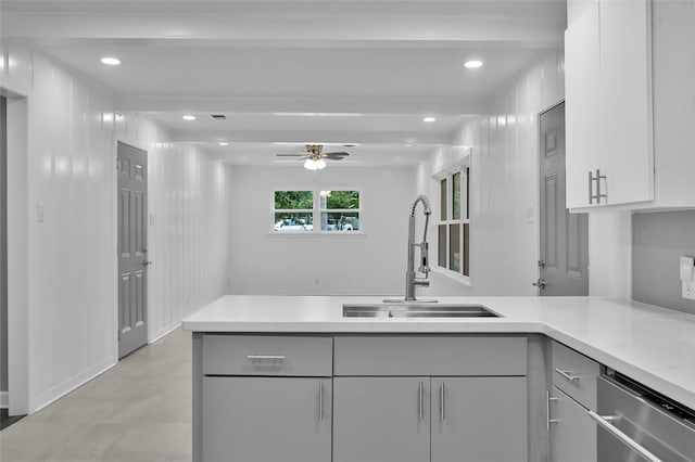 kitchen with light countertops, gray cabinetry, a sink, dishwasher, and a peninsula