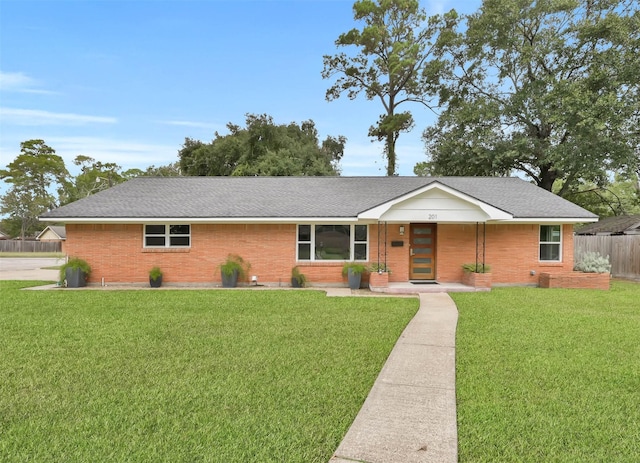 ranch-style home featuring brick siding, a front lawn, a shingled roof, and fence