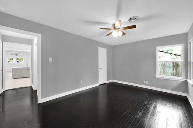 empty room featuring ceiling fan, baseboards, visible vents, and dark wood finished floors