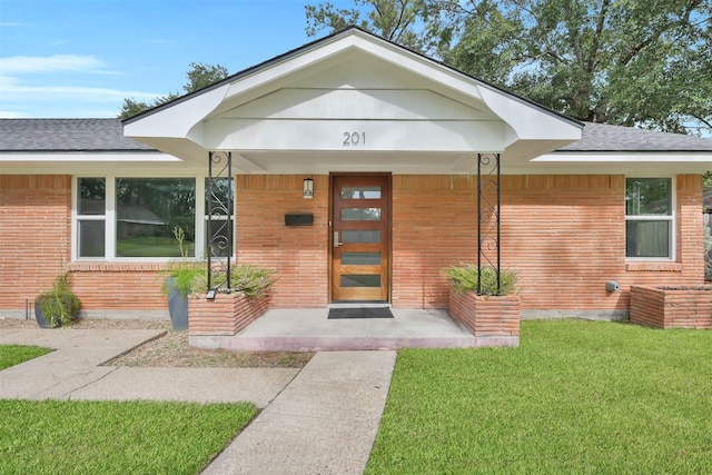 doorway to property with covered porch, a shingled roof, brick siding, and a yard